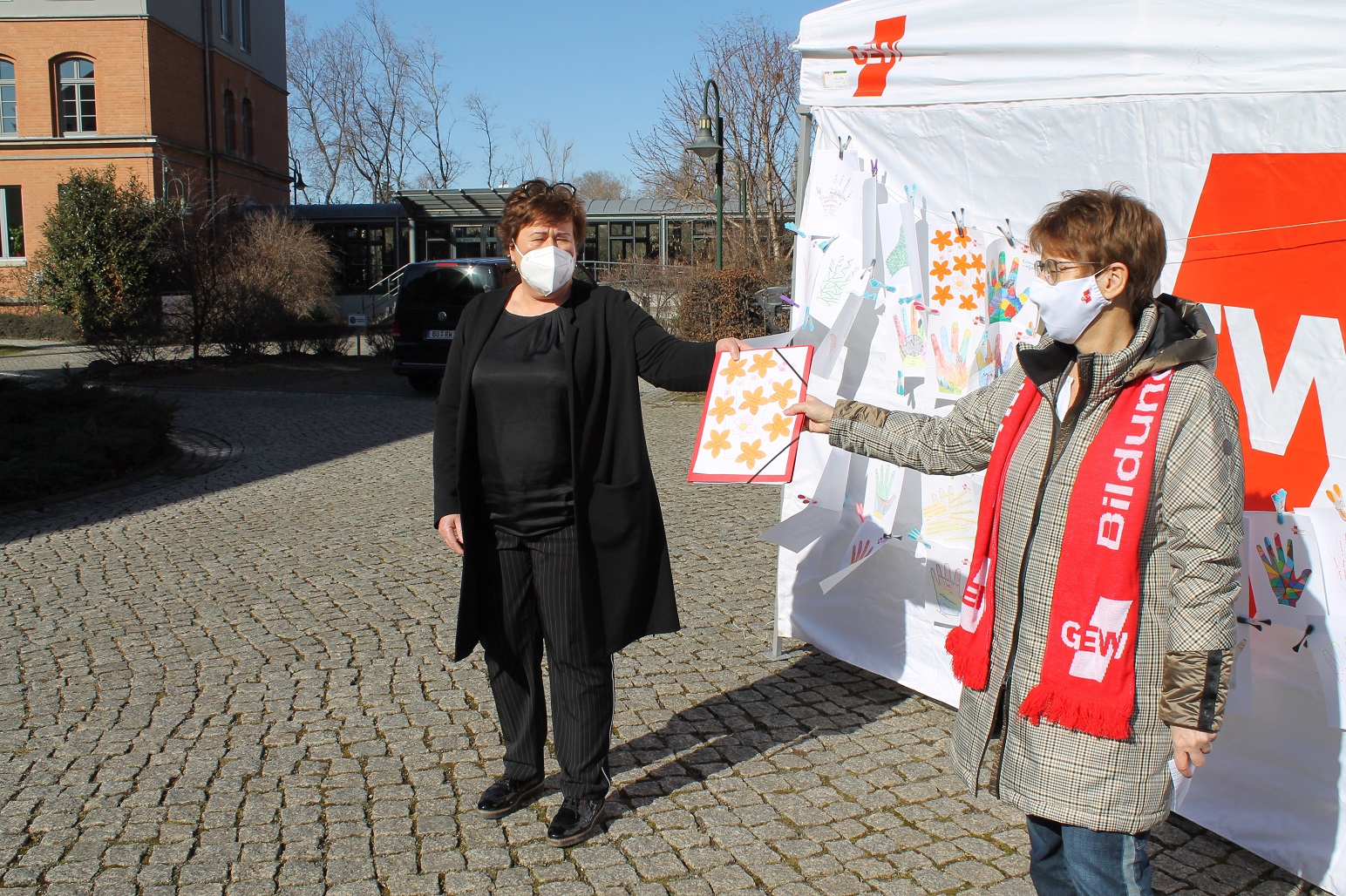 Eva Gerth von der GEW Sachsen-Anhalt übergibt die Mappe mit den bunt gestalteten Händen an Sozialministerin Petra Grimm-Benne. Foto: Frank Wolters